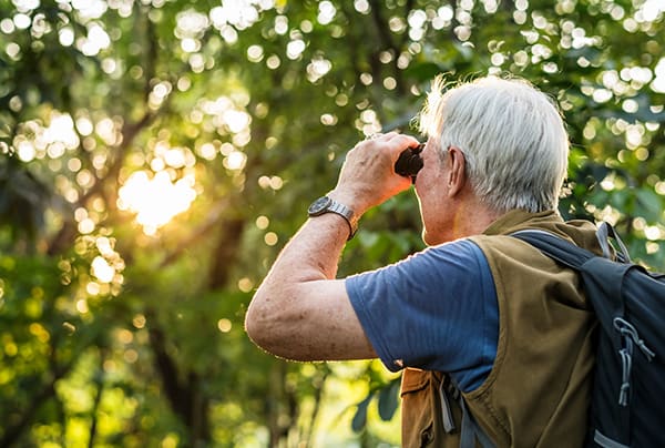A senior man looking through binoculars during a sunset