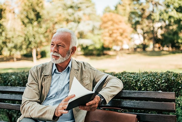 A senior man reading outdoors on a park bench